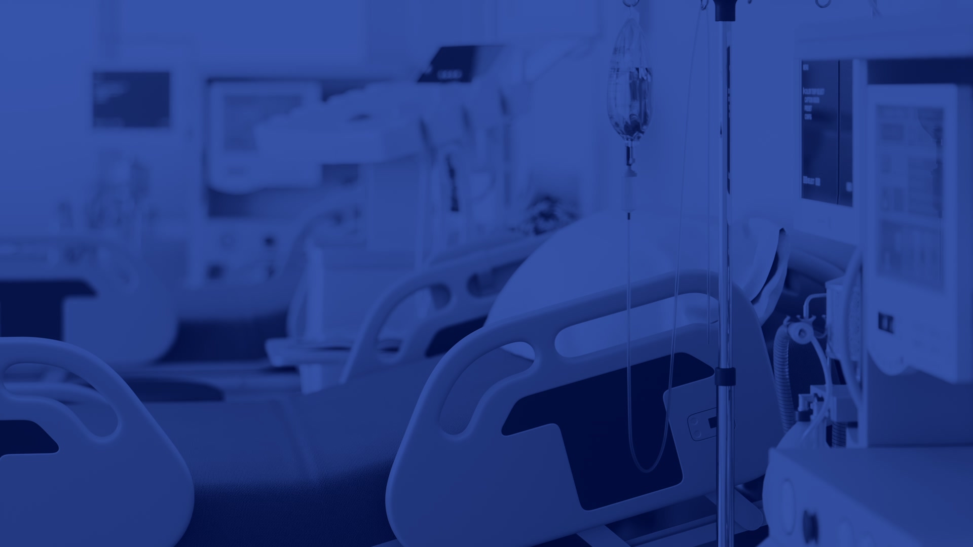 Interior of a hospital room with medical equipment including an IV stand, patient monitor, and a hospital bed in the foreground, conveying a sterile and professional healthcare environment.